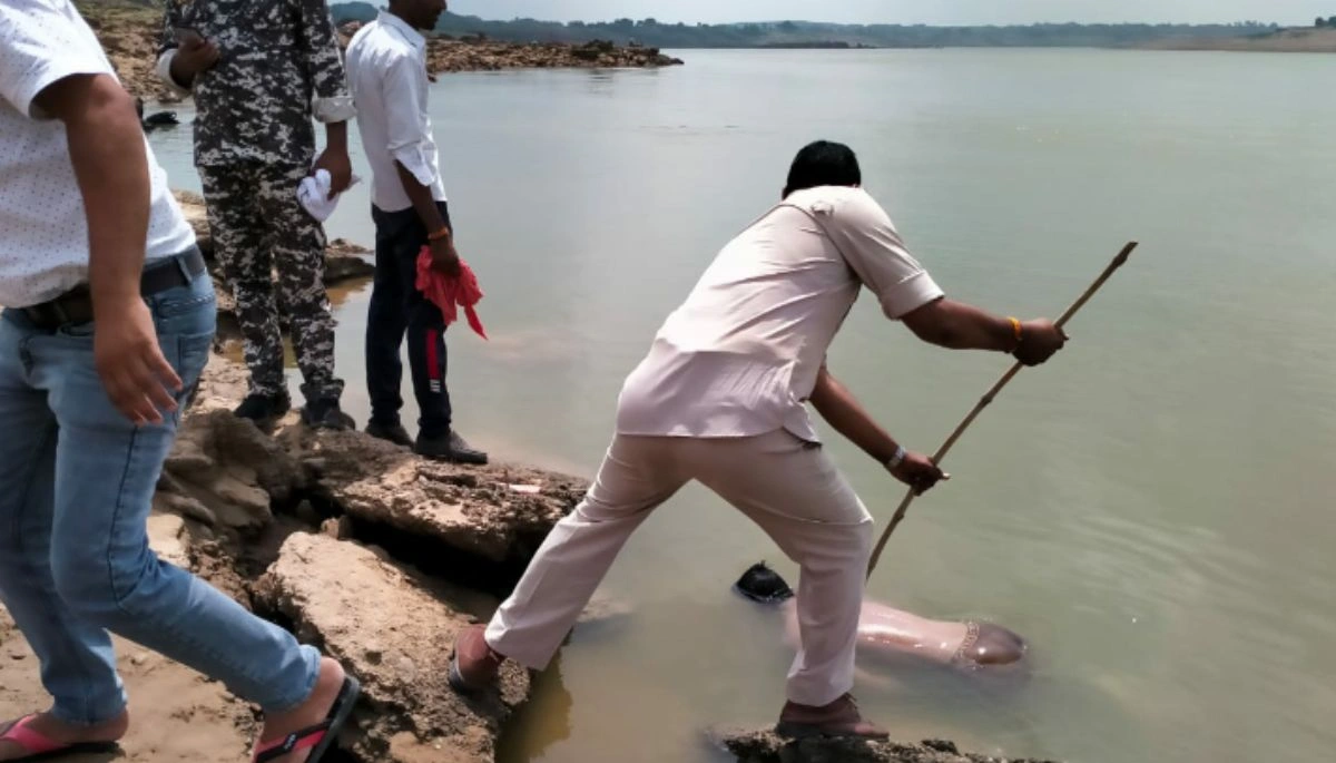 Police officers investigating the site near a riverbank where the body of an unidentified young woman was discovered, with surrounding bushes and forensic equipment visible.