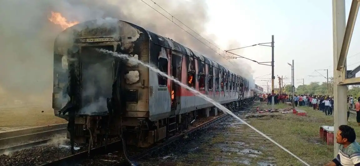 A train halted at a station during the night, with firefighters and railway staff working to control a fire in one of the train's coaches.